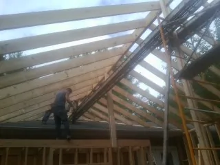 Rafters going up over a new addition with a worker on the wall in Chapin