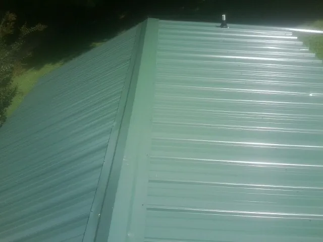 New green metal panels meeting at the ridge of a roof — Flat Roof Repair work by our crew in Chapin